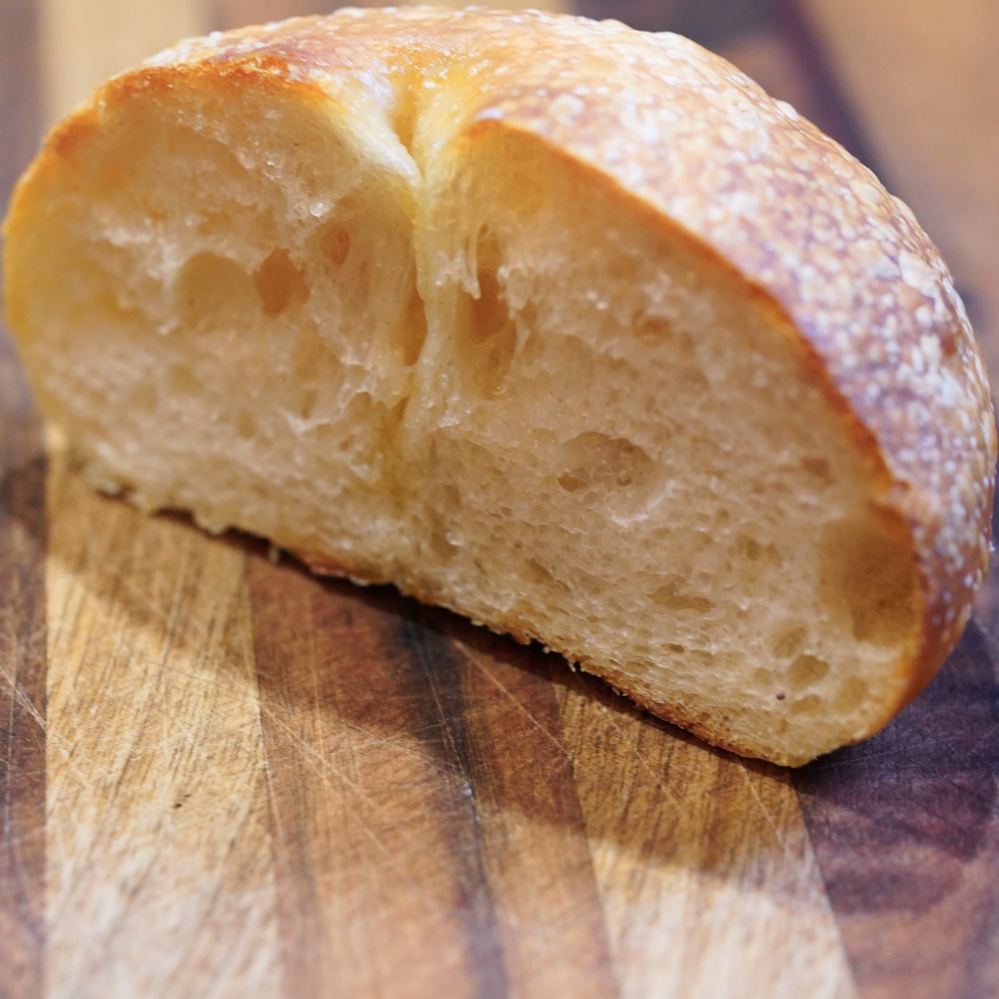 Half a nahly, cut side forward, on a wooden board — a thin, blistered golden crust and an open, glossy crumb, with no seeds or onion.